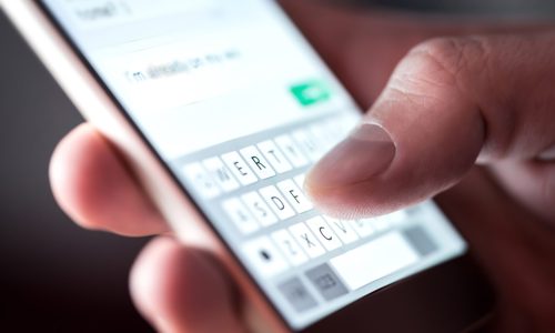 Man sending text message and sms with smartphone. Guy texting and using mobile phone late at night in dark. Communication or sexting concept. Finger typing with cellphone keyboard. Light from screen.