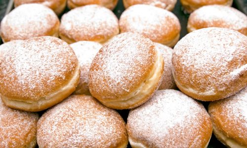 "Fresh baked German Jelly Doughnuts filled with strawberry jam or raspberry jam and dusted with powdered sugar. Full tray in a bakery counter display, delicious. Selective focus in foreground."