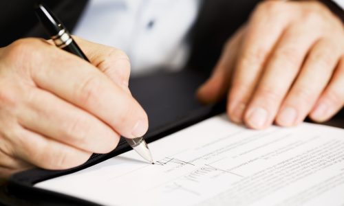 Businessman sitting at office desk signing a contract with shallow focus on signature.